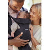 parents admiring infant while babywearing a baby bjorn carrier free anthracite