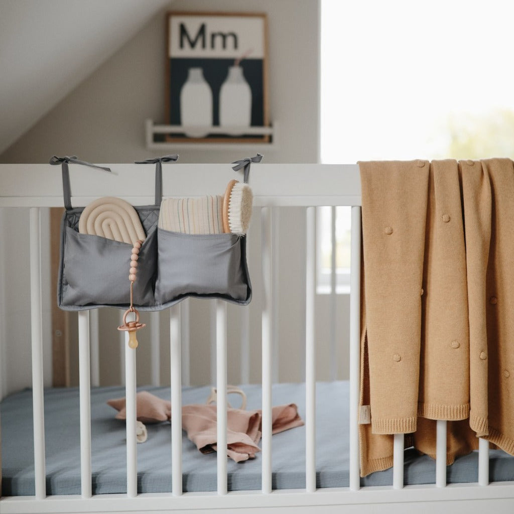 baby crib with mushie product hanging on rail with yellow blanket