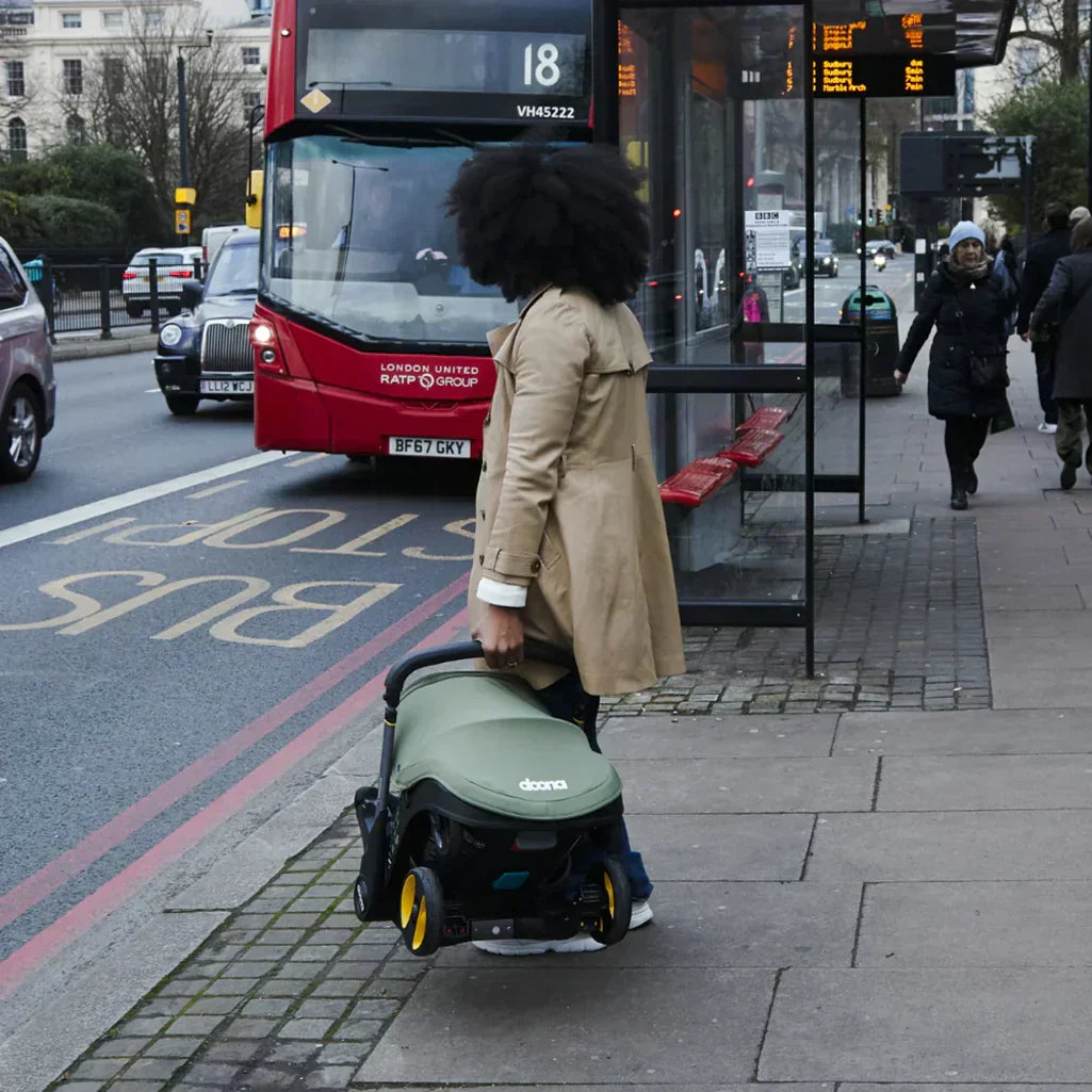 stylish mother holding onto doona x infant safe car seat and stroller travel system on city street