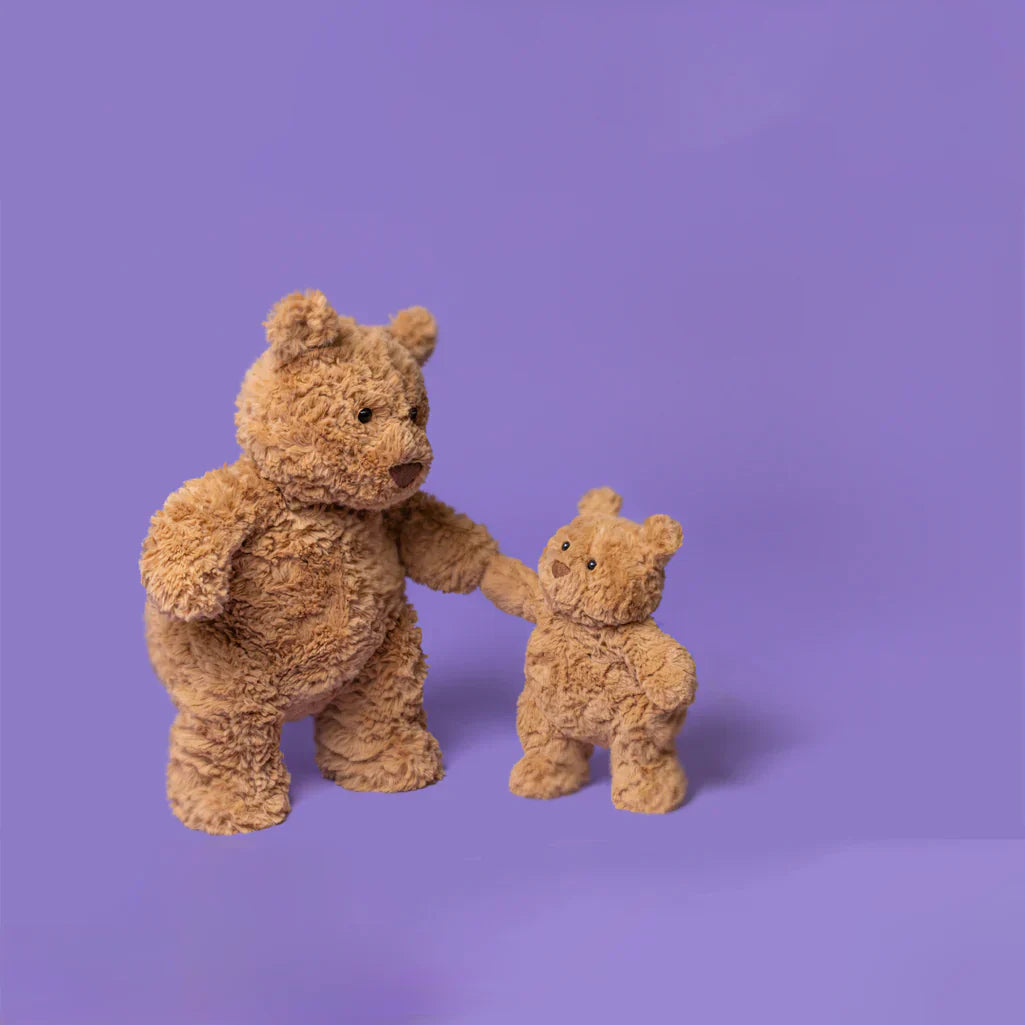two jellycat bartholomew bears on purple background holding paws