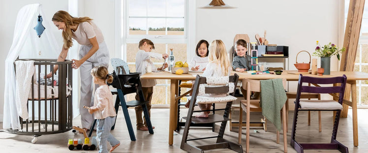 Mom Checking on Baby While Kids Sit Around Table in High Chairs