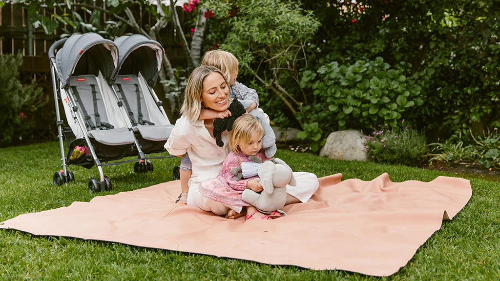Mom Playing at a Park with Two Kids on a Quilt with G-Link Stroller in the Background