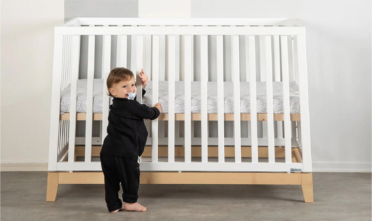 Baby Standing in Front of Modern White Crib