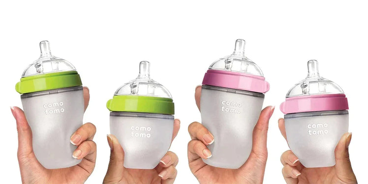 Hands Holding Up Four Comotomo baby Bottles in Green and Pink