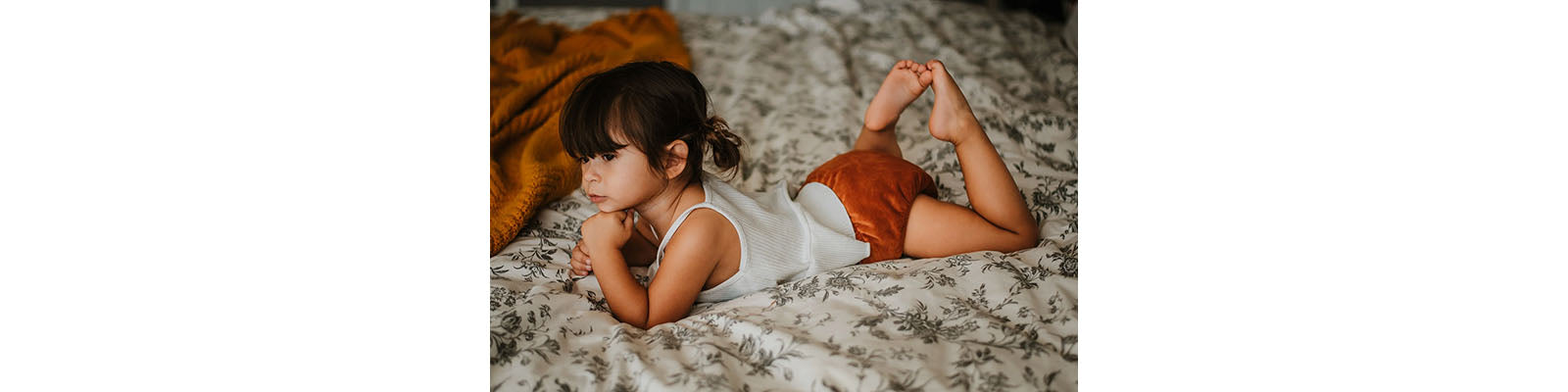 Child Resting on Bed wearing Orange Cloth Diaper