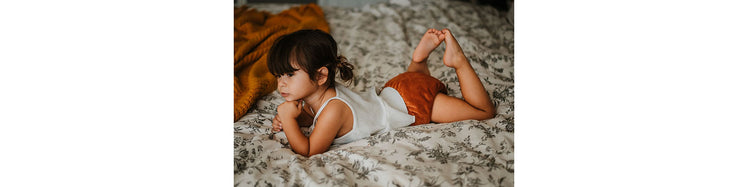 Child Resting on Bed wearing Orange Cloth Diaper