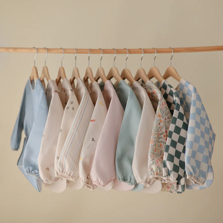A variety of Mushie Long Sleeve Bibs in neutral and pastel shades, perfect baby bibs for mealtime messes.