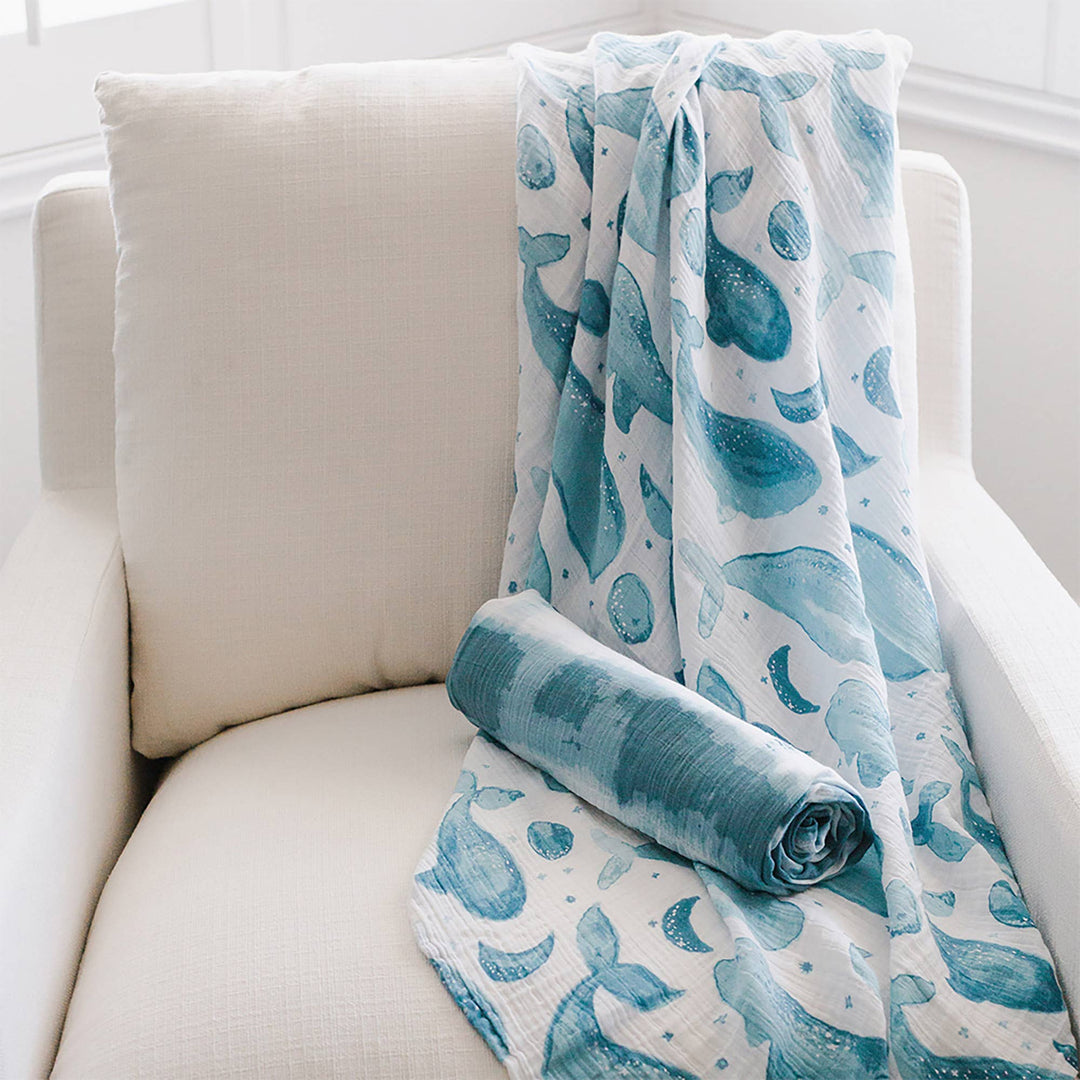 soft water color blue whale muslin organic cotton crane baby newborn swaddle set on white chair 