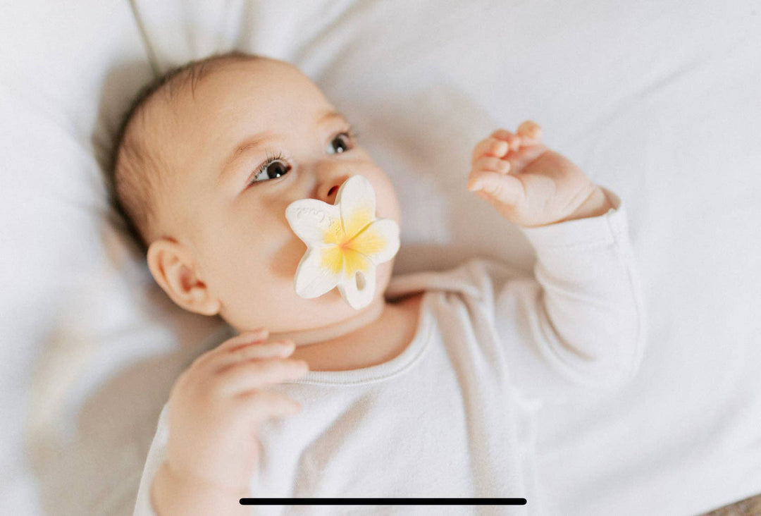 A baby chews on the Oli & Carol Hawaii the Flower teether while lying down