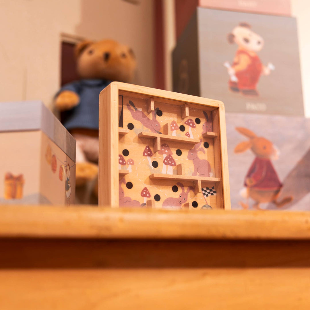 This Egmont maze leans near a teddy bear, showing the Mini Wooden Labyrinth in a cozy nursery scene