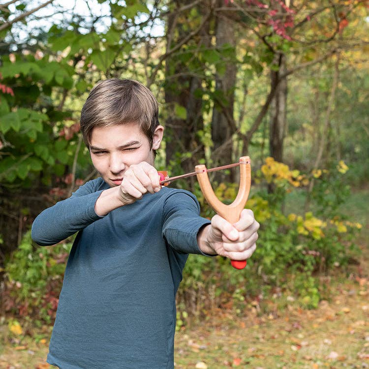 Child playing with Huckleberry Slingshot outdoor toy in wooded area