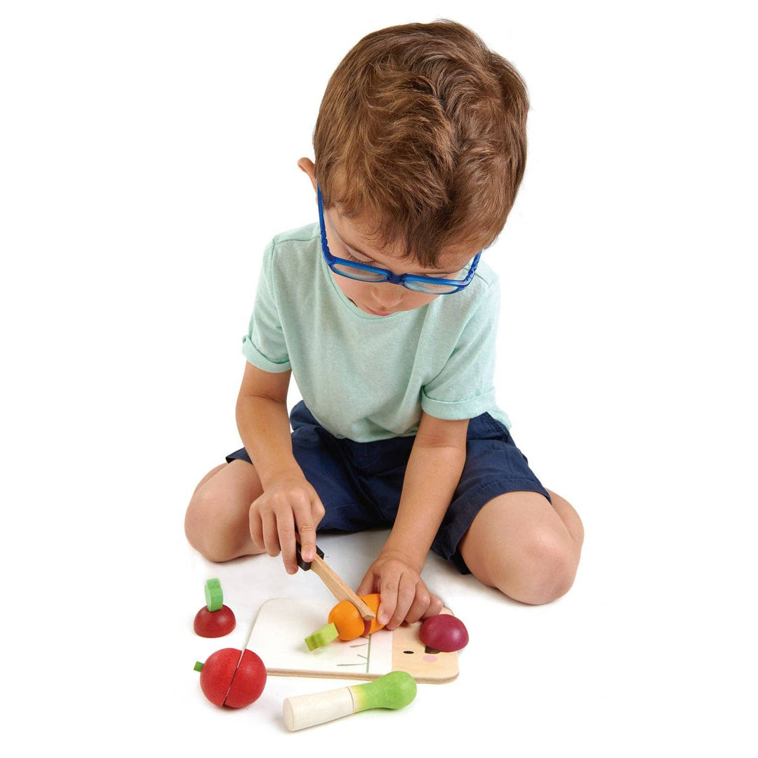 A toddler practices pretend cooking skills with the Tender Leaf Toys Mini Chef Chopping Board