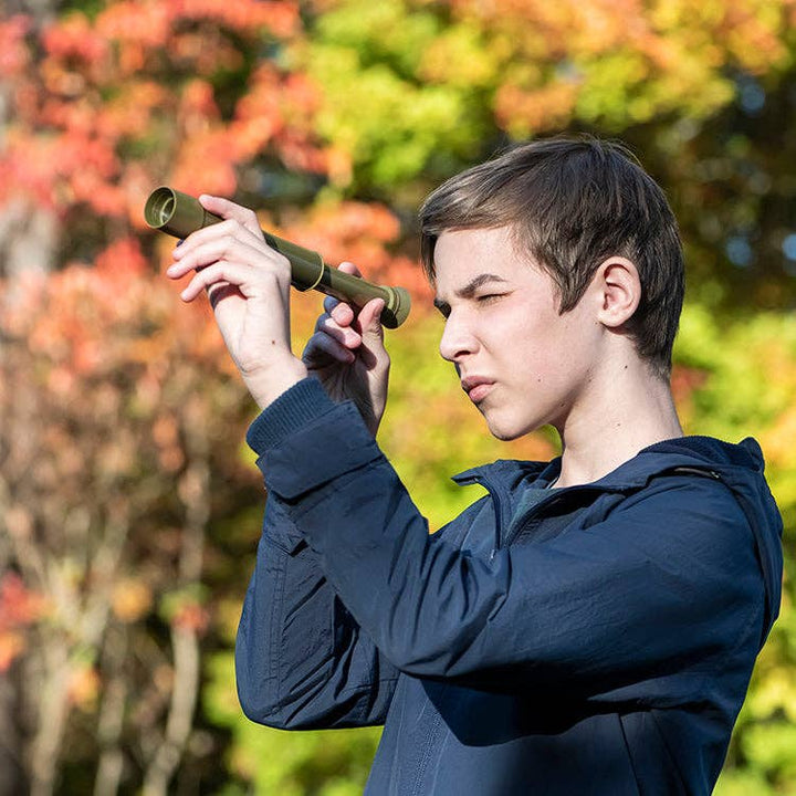 Child using Huckleberry Telescope outdoor educational toy outdoors with trees in background