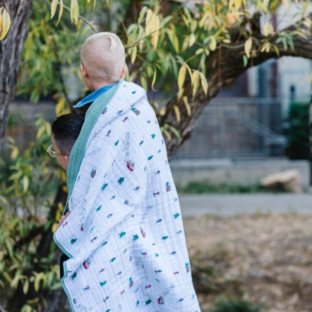 Little Unicorn Original Cotton Muslin Quilt - Powder Party draped over a crib, a charming baby quilt that adds warmth and playful design.