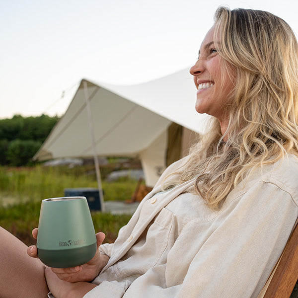 Smiling camper holding Klean Kanteen 10oz Rise Wine Tumbler in Sea Spray, crafted from non toxic materials