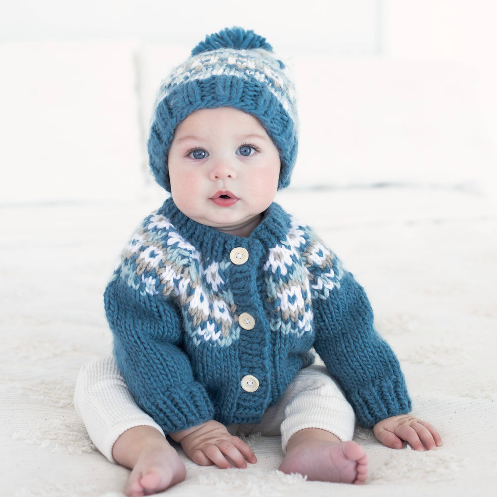 Baby in Huggalugs Fairisle Slate cardigan and matching beanie, sitting barefoot