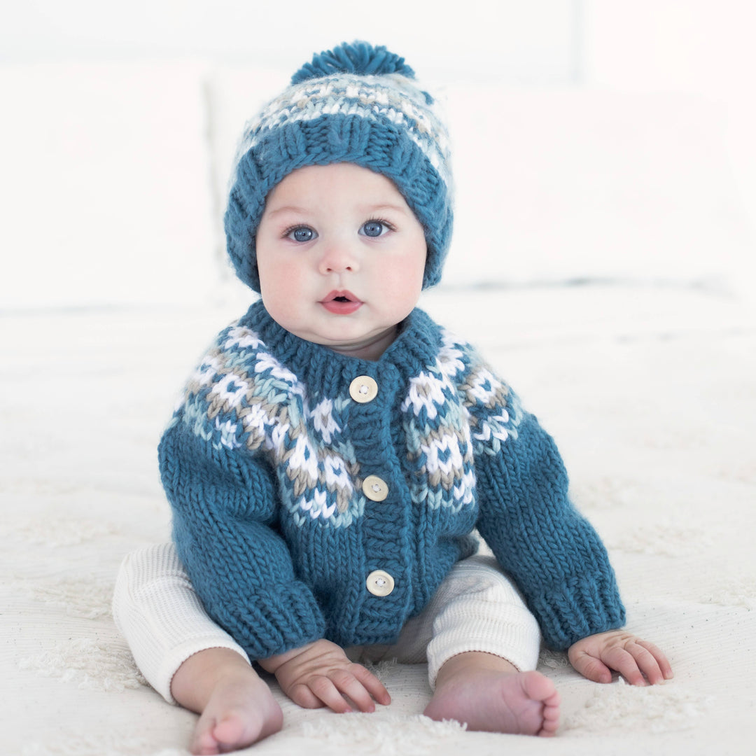 Baby in Huggalugs Fairisle Slate cardigan and matching beanie, sitting barefoot