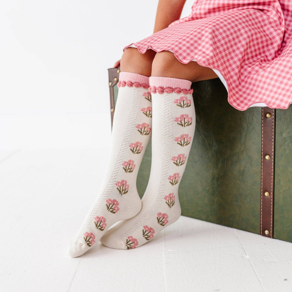 Baby wearing Little Stocking Co. Posie Knee Socks in Old Rose with a pink gingham dress, floral knee-high socks