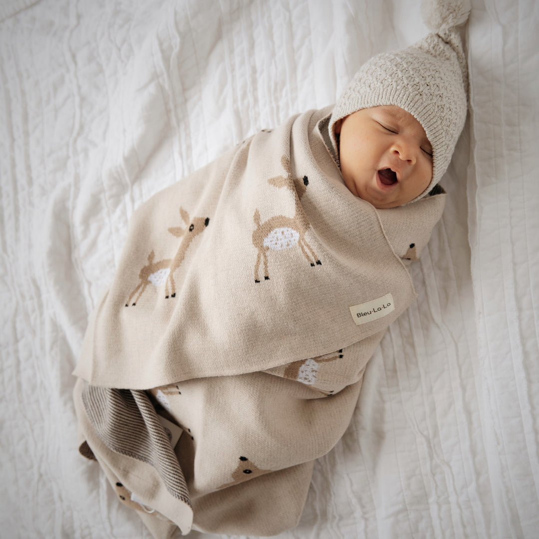 Sleeping infant wrapped in a Bleu La La deer knit swaddle blanket, soft cotton designed for gentle newborn sleep
