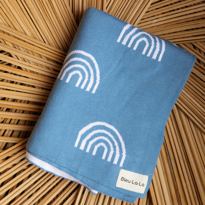 Soft Cotton Swaddle Bleu La La Rainbow Blanket in Blue against a wooden background