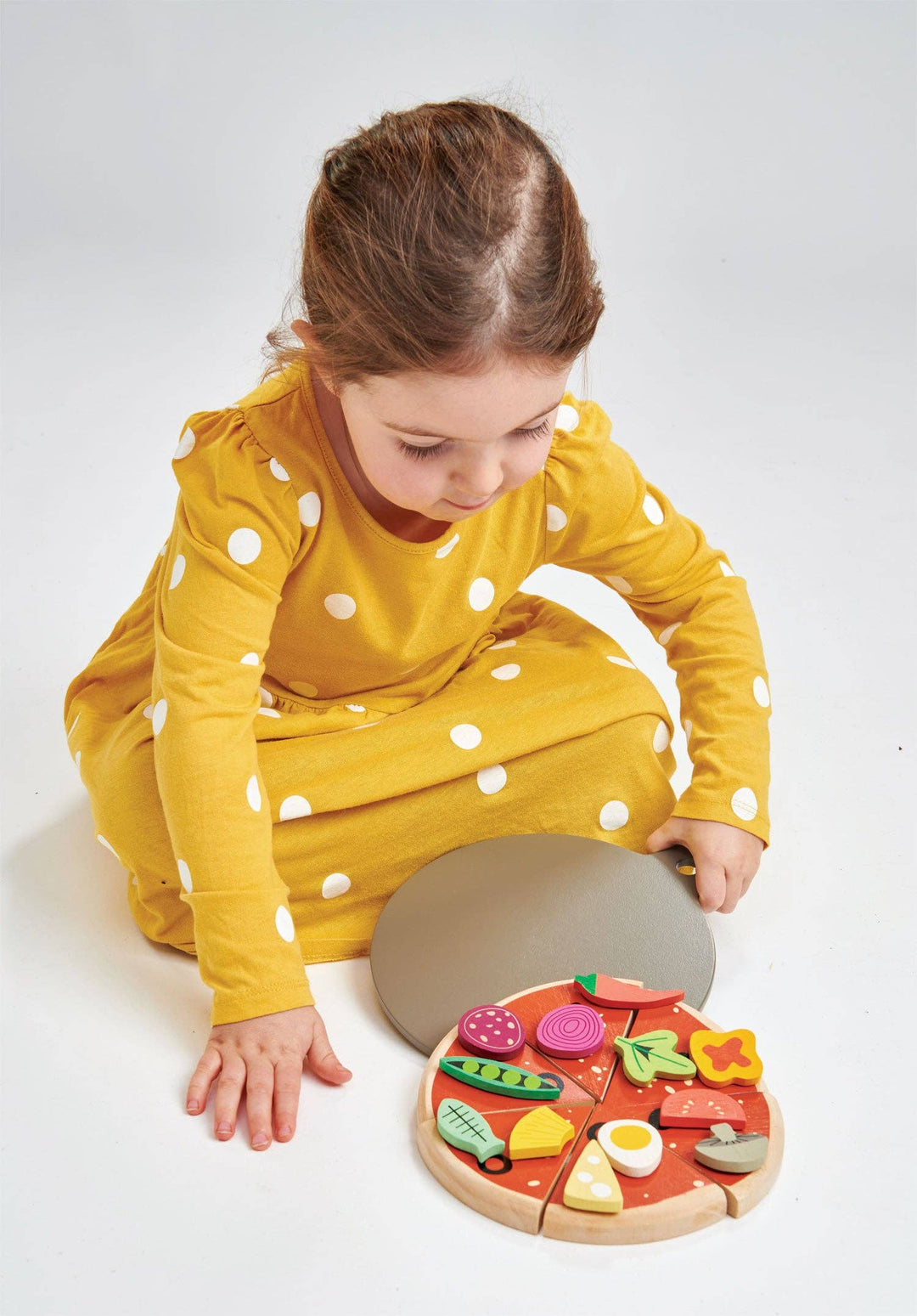 A young girl in yellow pajamas kneels beside her Tender Leaf Toys Pizza Party