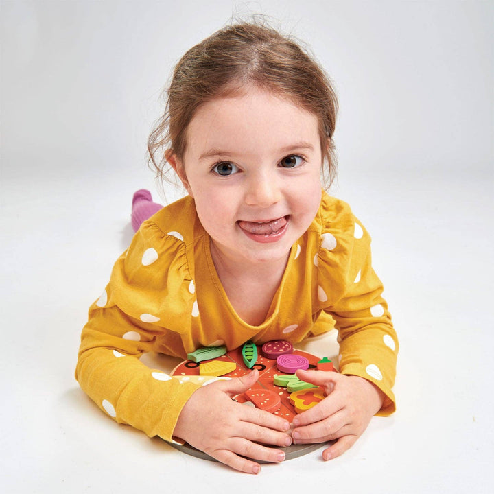 Smiling girl holds up a topping piece from the Pizza Party toy by Tender Leaf Toys