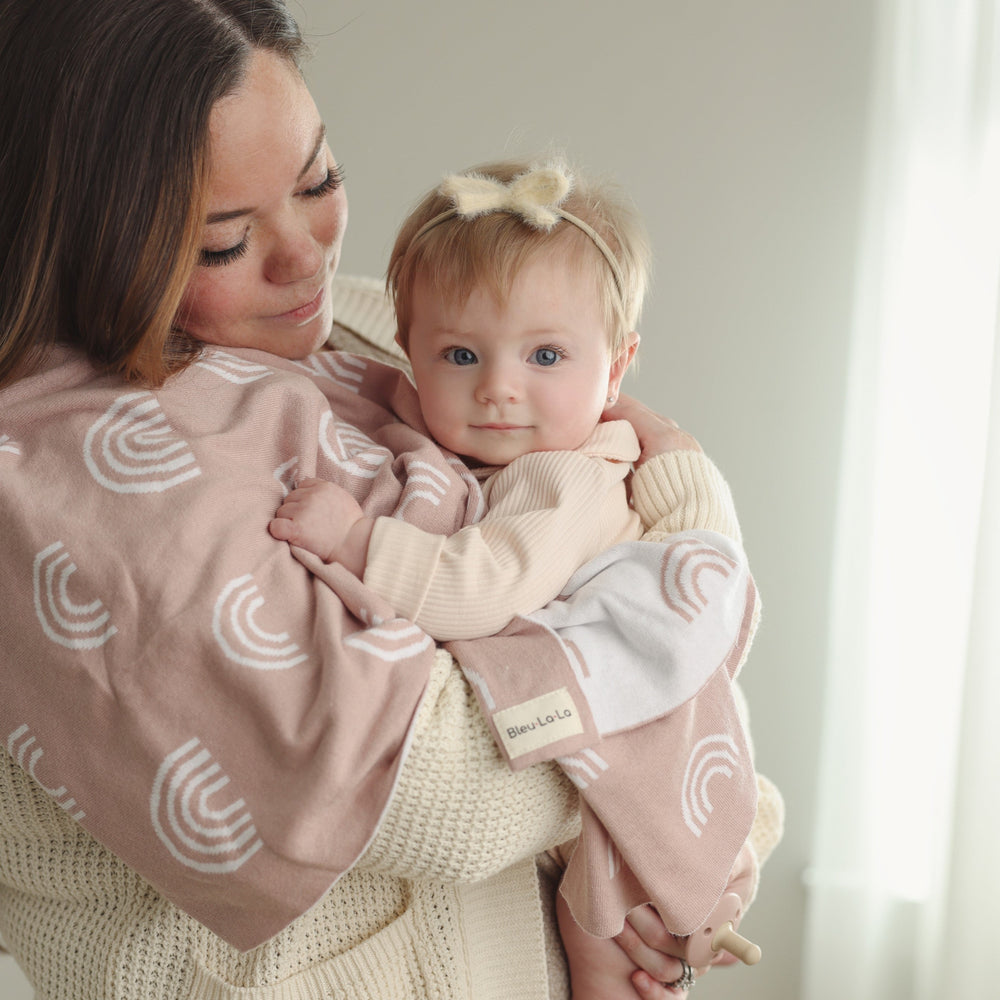 Woman holding baby wrapped in the Bleu La La Rainbow Blanket in Pink