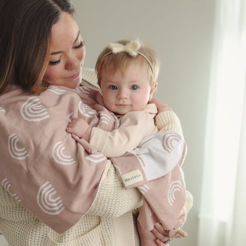 Woman holding baby wrapped in the Bleu La La Rainbow Blanket in Pink
