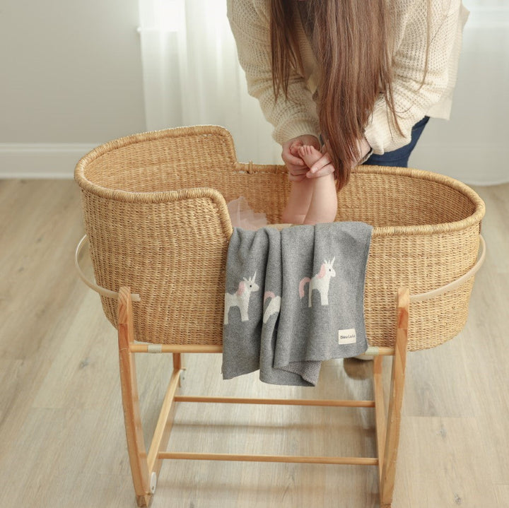 Baby resting in a bassinet wrapped in a Bleu La La knit unicorn blanket, cozy cotton for naps and sleep