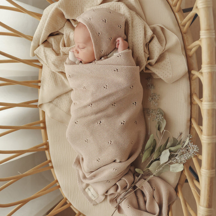 Newborn swaddled in Bleu La La Organic Pointelle Luxury Knit Swaddle Blanket in oatmeal inside a woven bassinet.