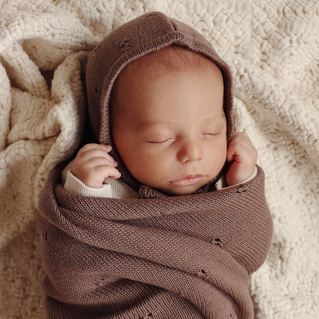 Newborn sleeping swaddled in Bleu La La Organic Pointelle Luxury Knit Swaddle Blanket in milk chocolate for breathable comfort.
