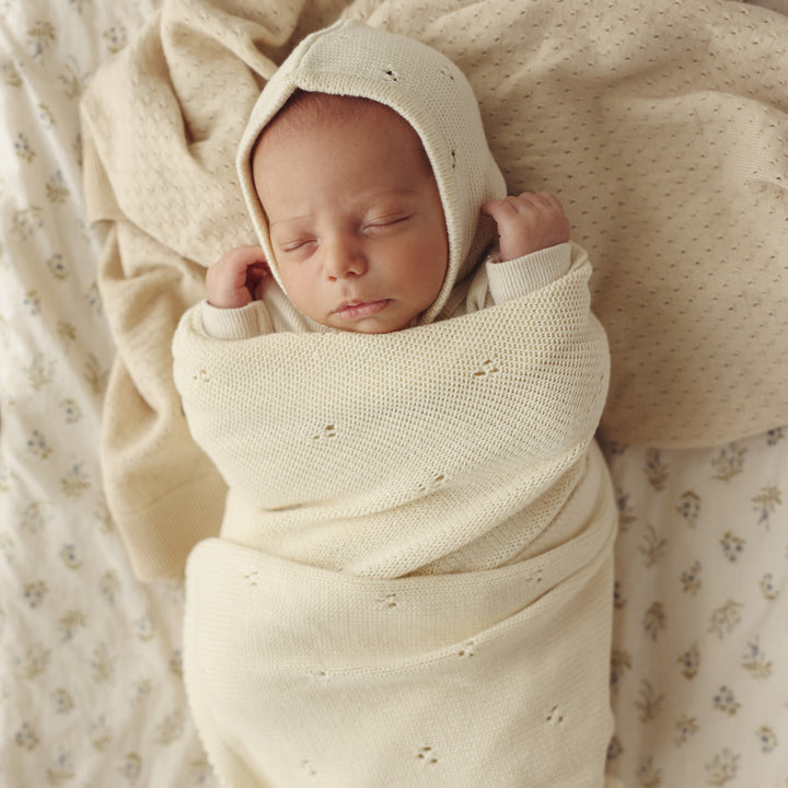 Newborn swaddled in Bleu La La Organic Pointelle Swaddle Blanket in butter cream for gentle breathable organic cotton comfort.