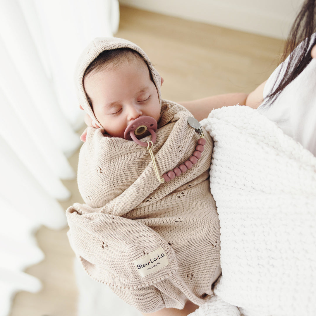 Parent cradling baby wrapped in Bleu La La Organic Pointelle Swaddle Blanket in oatmeal for lightweight year-round use.