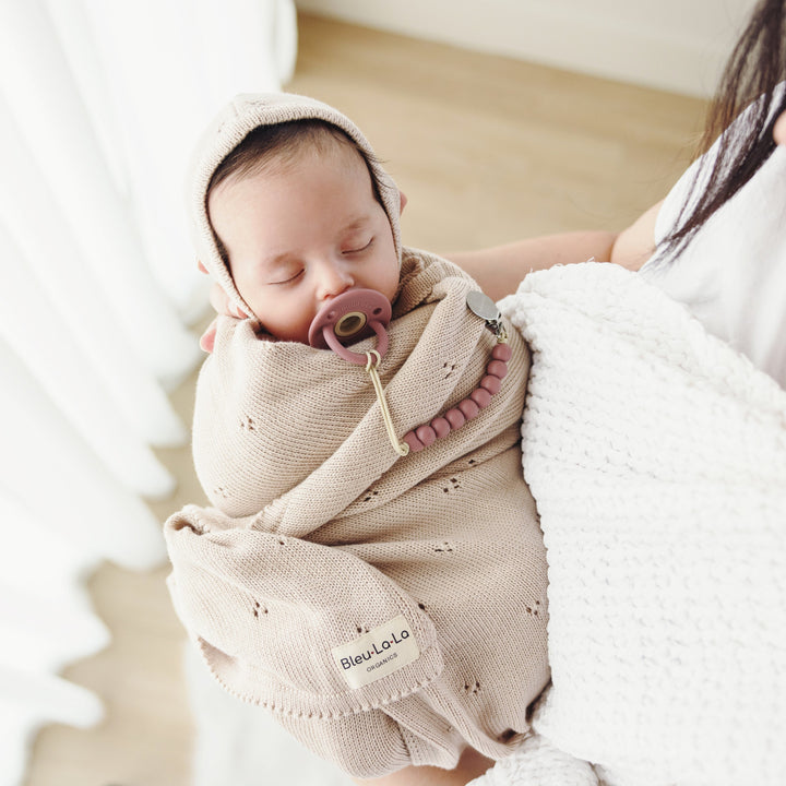 Parent cradling baby wrapped in Bleu La La Organic Pointelle Swaddle Blanket in oatmeal for lightweight year-round use.