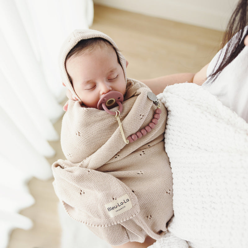 Parent cradling baby wrapped in Bleu La La Organic Pointelle Swaddle Blanket in oatmeal for lightweight year-round use.