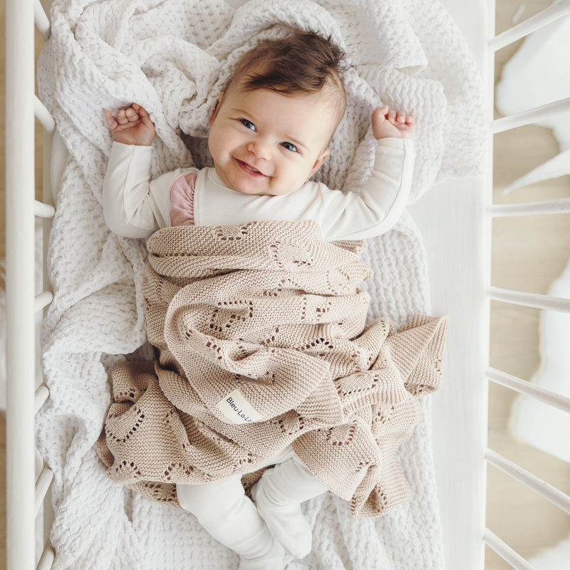 Baby holding Bleu La La 100% Cotton Luxury Knit Heart Swaddle Baby Blanket in oatmeal, showcasing lightweight breathable cotton.