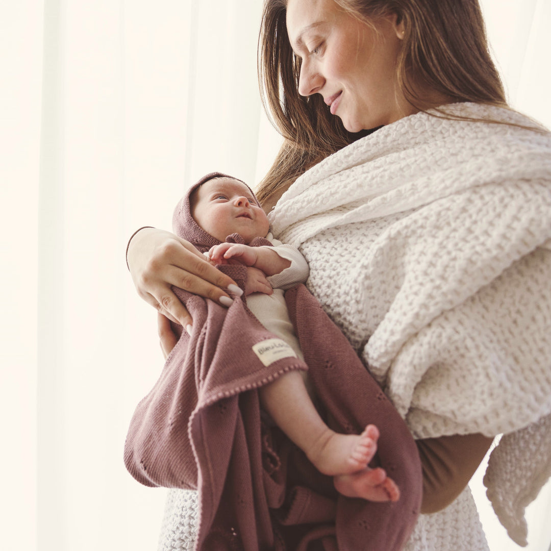 Parent holding baby wrapped in Bleu La La Organic Pointelle Swaddle Blanket in sugar plum for soft everyday cuddles.