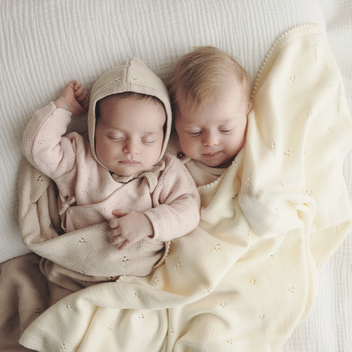 Two newborns cuddled together on Bleu La La Organic Pointelle Swaddle Blanket in oatmeal and in butter cream for cozy breathable comfort.