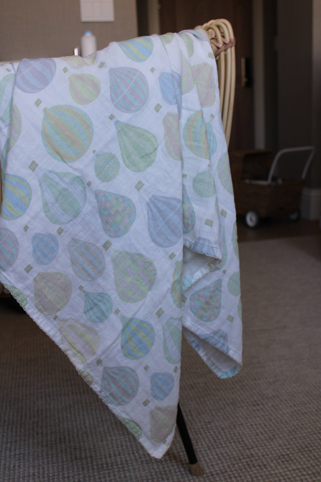 Little Threads pastel air balloon muslin blanket draped over crib, lightweight baby swaddle for stroller cover, nursing, and nursery use