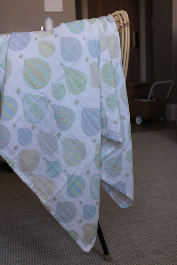 Little Threads pastel air balloon muslin blanket draped over crib, lightweight baby swaddle for stroller cover, nursing, and nursery use