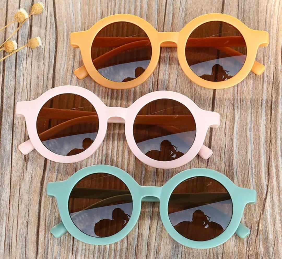 three boho babe round circle tinted sunglasses in yellow, sage, and pink on wooden table