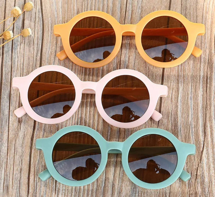 three boho babe round circle tinted sunglasses in yellow, sage, and pink on wooden table