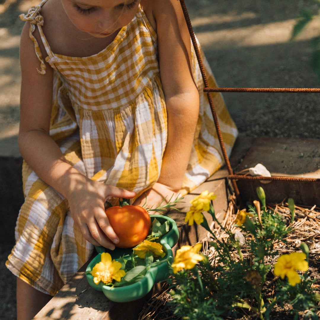 A little girl gardens outdoors while holding her Oli & Carol Kendall the Kale plate