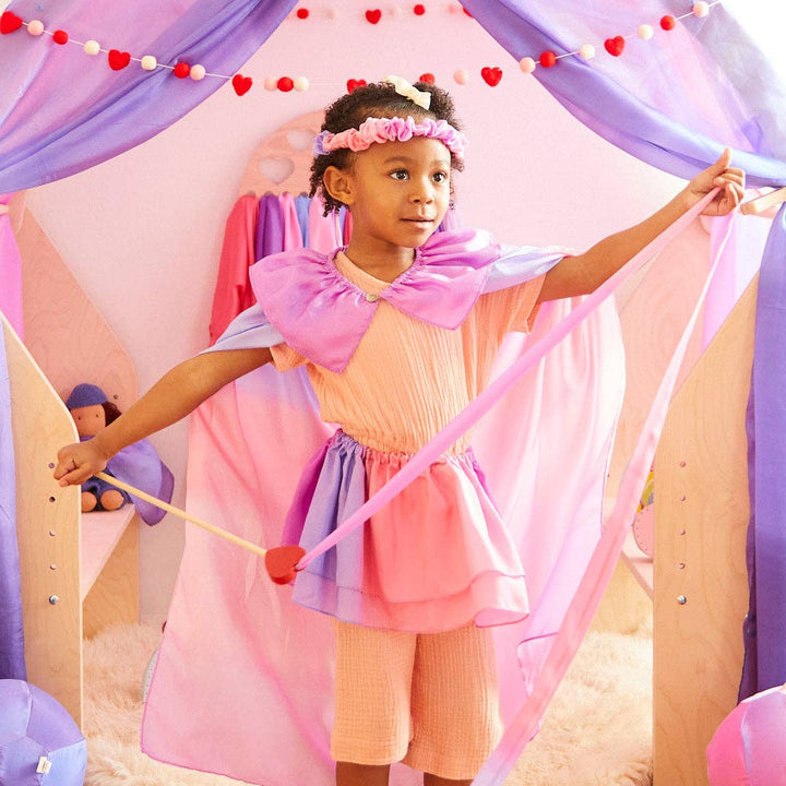 A child twirls in the Sarah's Silks Blossom Garland, arms spread wide during pretend play