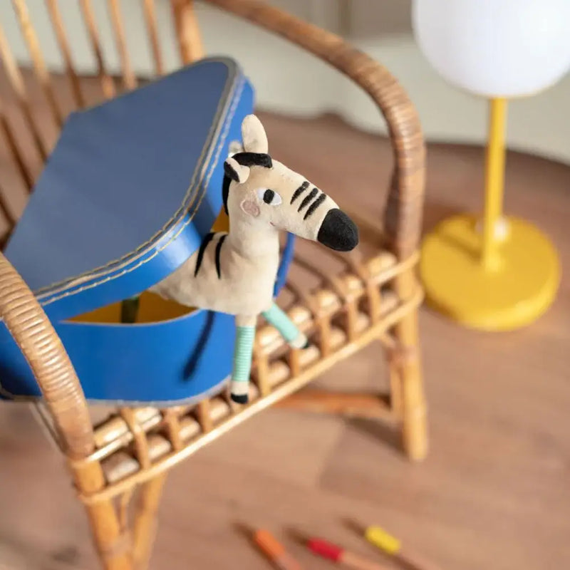 Moulin Roty Zebra Rattle The Toupitis Plush zebra rattle toy in a blue suitcase on a chair