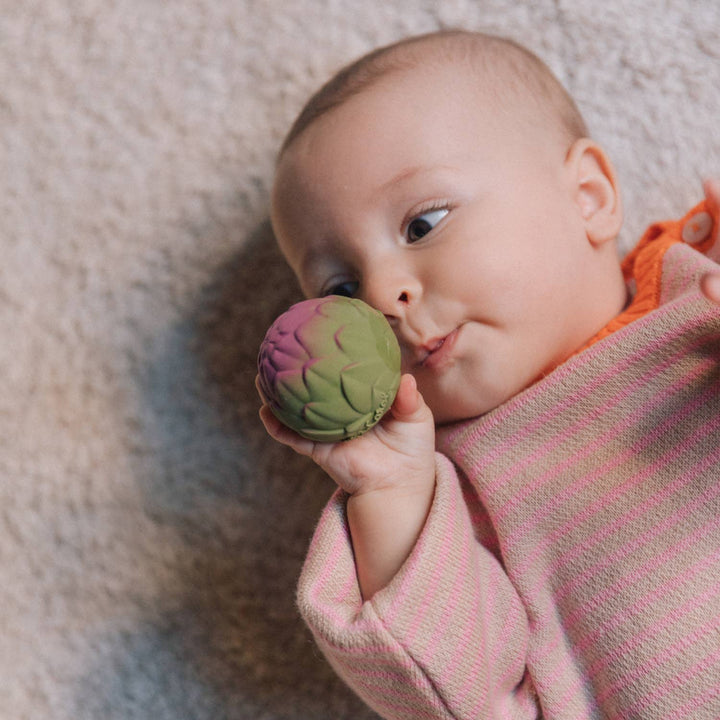 A baby chews on an artichoke ball from the Oli & Carol Veggie Soup Baby Sensory Balls