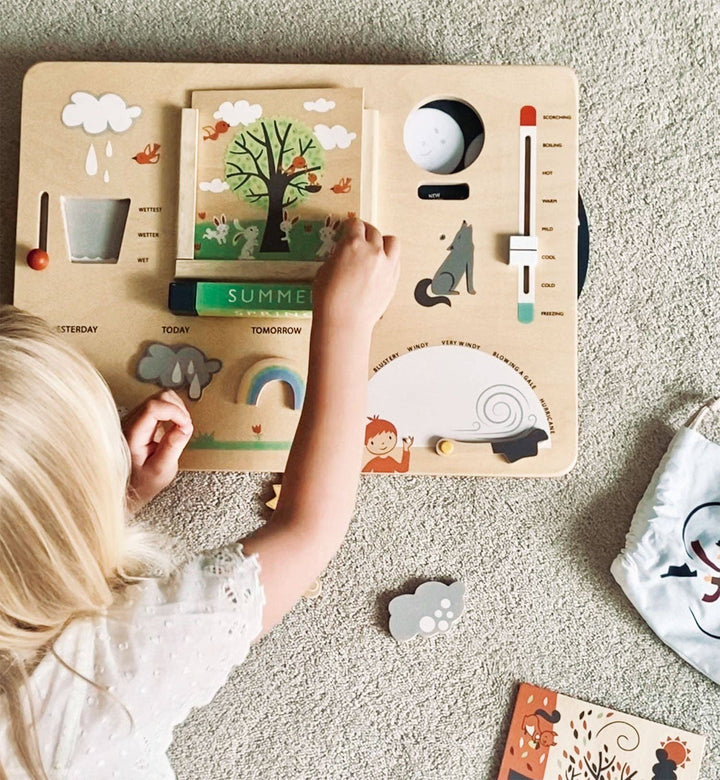 A young girl places a weather icon onto the Tender Leaf Toys Weather Watch board