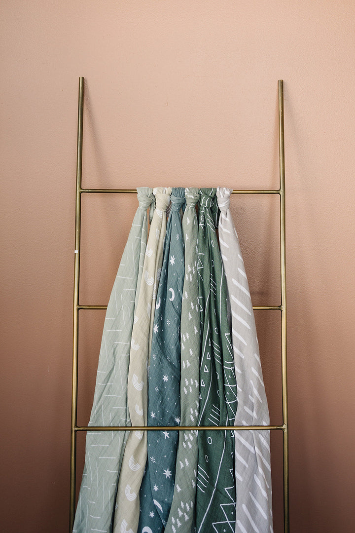 Mebie Baby Pines Muslin Swaddle Blanket held up to show the soft stretch fabric.