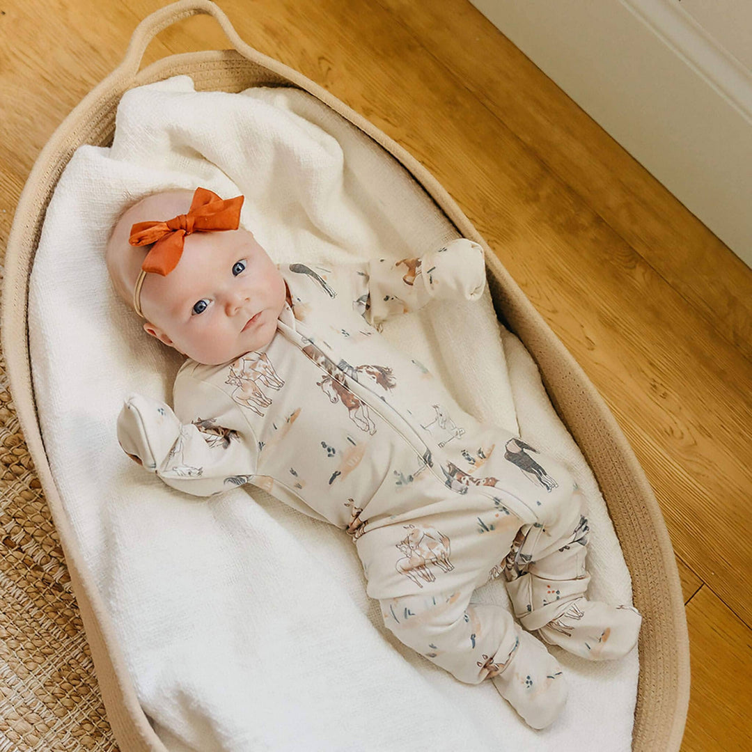 Copper Pearl Montana zip-up footie pajama on baby in bassinet, soft bamboo baby sleepwear for newborn comfort and easy diaper changes