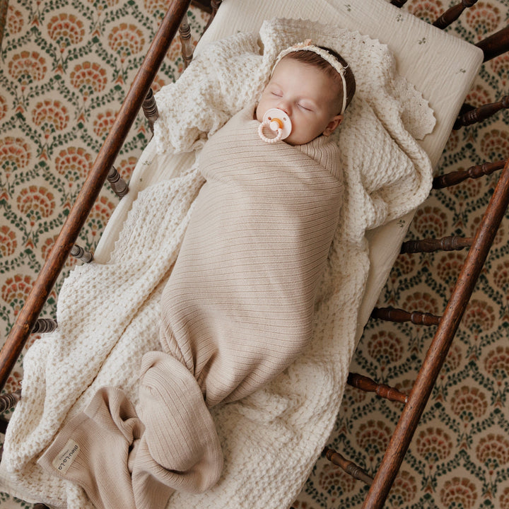 Baby wrapped in pink Bleu La La Organic Ribbed Knit Cotton Baby Blanket on cream bedding, soft organic cotton newborn swaddle